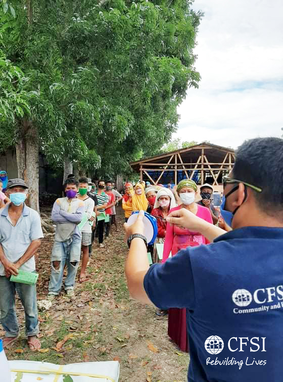 CFSI staff (right) instructs beneficiaries to observe proper social distancing before the distribution.