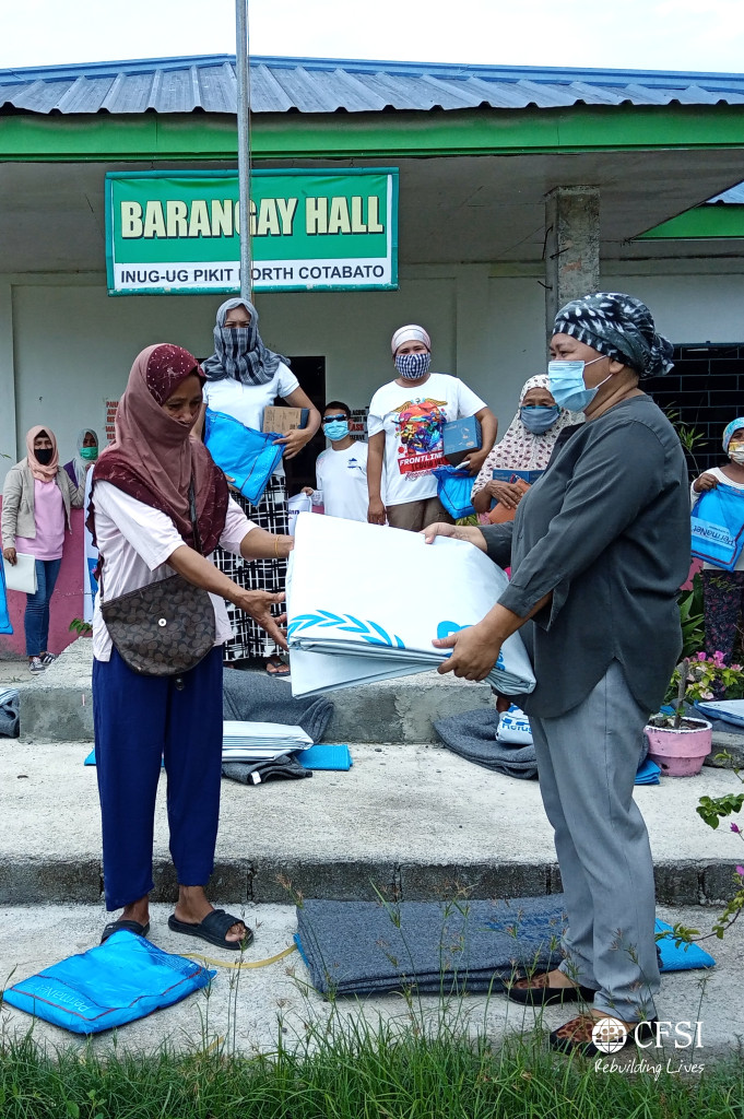 Barangay Inug-ug official (right) hands over core relief items to one of the internally displaced persons (left) who took refuge in the evacuation center.